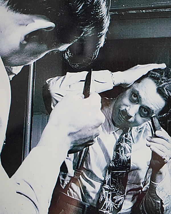 Fotografía antigua en blanco y negro de un barbero con navaja junto a un cliente que se mira al espejo